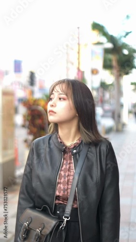 Vertical video of a young Japanese Okinawan woman in her 20s walking on Kokusai Street, a tourist attraction in Naha City, Okinawa Prefecture 沖縄県那覇市の観光名所の国際通りで若い２０代の日本人沖縄県民女性が歩く縦長動画 photo