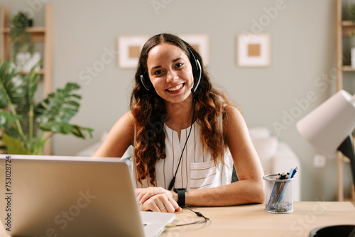 Young businesswoman with headset in office with laptop on table looking at camera