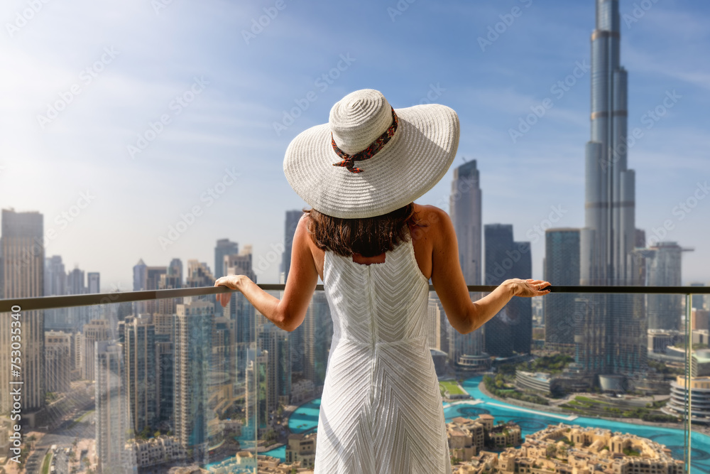 Fototapeta premium A elegant luxury woman with a white hat enjoys the view over the Downtown City skyline of Dubai, UAE