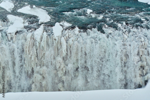 Majestic frozen waterfall with icicles and snow viewed from the side of a cliff. Location: Gullfoss Falls, Iceland.