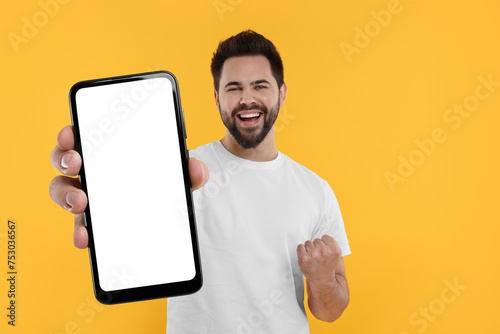 Happy man holding smartphone with empty screen on orange background