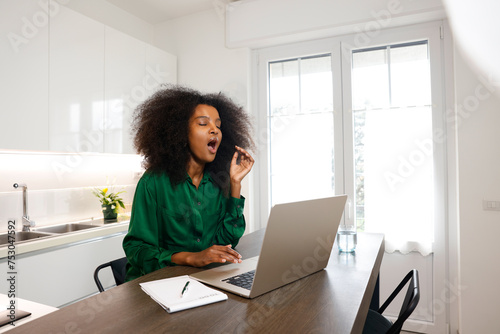 A black girl with afro hair yawning feeling tired and sleepy after all of work at home  photo