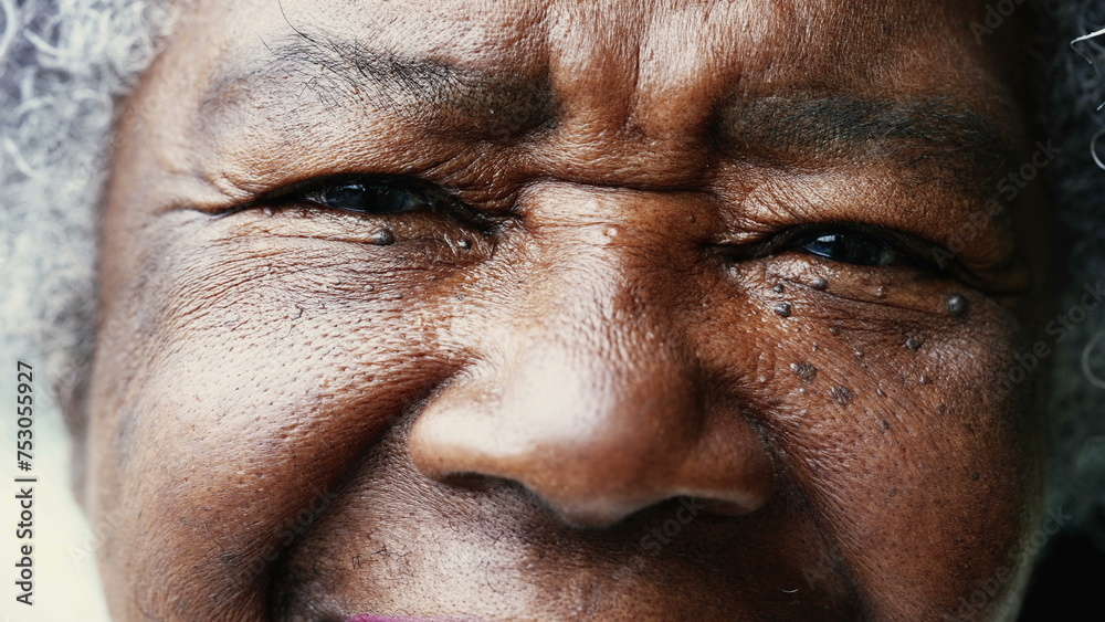 Obraz premium One happy black senior woman tight macro close-up of eyes and face looking at camera smiling. Wrinkled African American person in 80s showing wisdom and old age