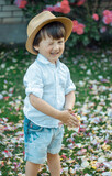 a robber boy in a hat winks mischievously at the camera, in his hands he holds an armful of rose petals, rose garden, green grass, summer evening