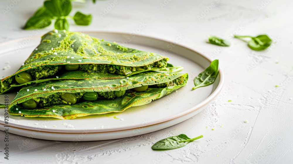 Obraz premium Spinach green pancakes crepes with green beans on a plate on white background. Trendy vegetarian food. Healthy breakfast recipe. Plant based diet concept. Restaurant menu