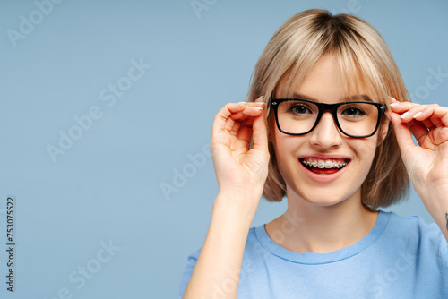 Blonde woman with braces  wearing eyeglasses smiling and looking at camera