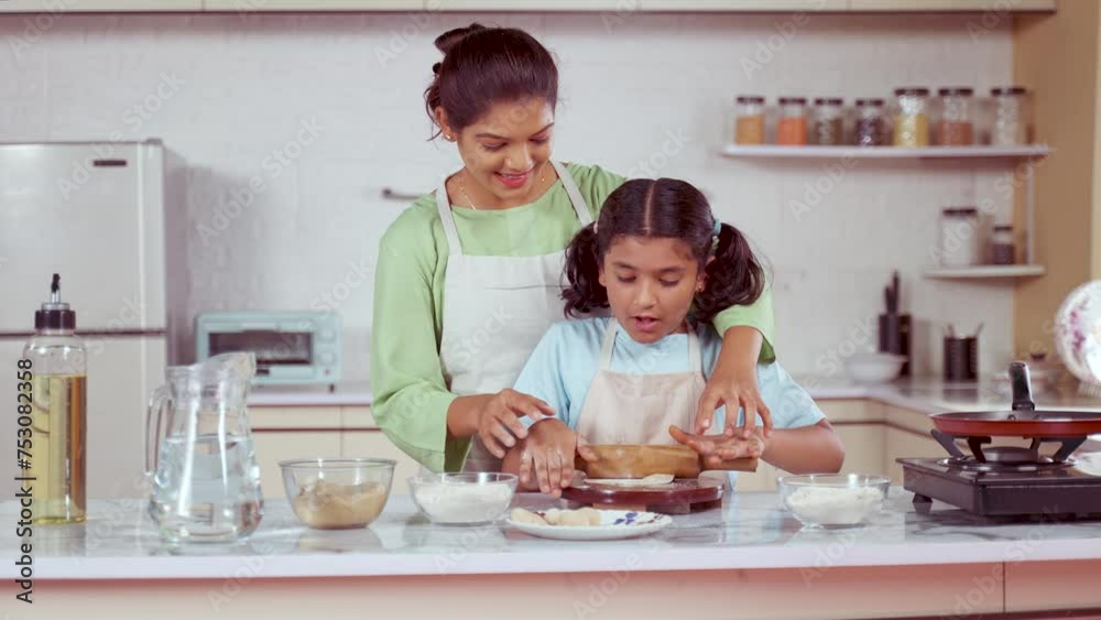 happy Indian mother teaching cooking by making chapati by holding hands at kitchen - concept of fun learning, family bonding and motherhood. happy Indian mother teaching cooking by making chapati by holding hands at kitchen - concept of fun learning, family bonding and motherhood.