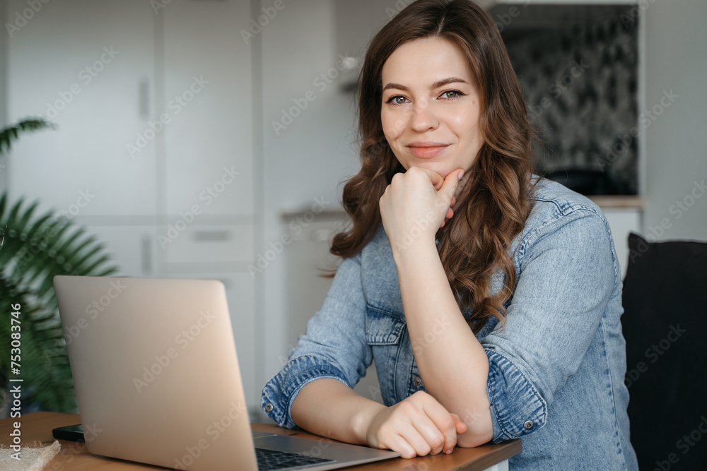 A woman is seated at a table with a laptop computer and a plant, smiling A woman is seated at a table with a laptop computer and a plant, smiling