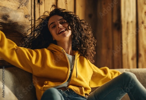 Beautiful curly girl in blue earphones and yellow hoodie  listen music on the sofa at wooden background  photo