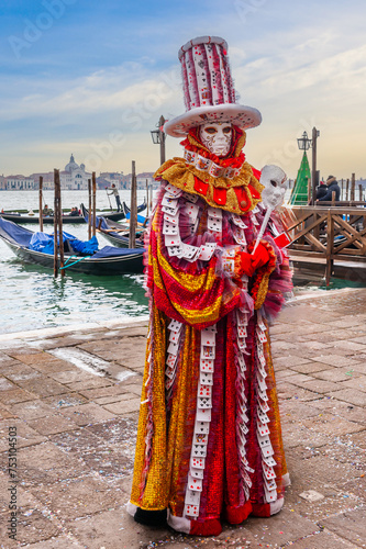A person dressed for carnival in front of the gondolas and the Venetian lagoon in Veneto, Italy