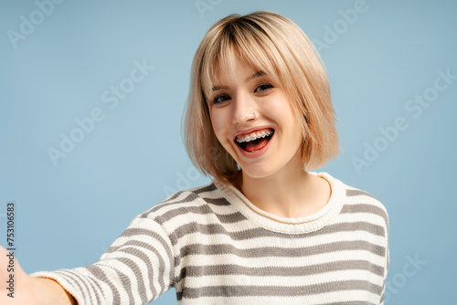 Beautiful caucasian woman with blond hair with braces taking selfie, looking at camera