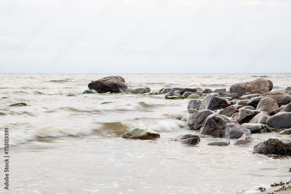 coastline with red and green rocks on the right side and breezy waves with light grey sky on the left and in the background coastline with red and green rocks on the right side and breezy waves with light grey sky on the left and in the background