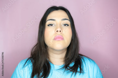 Close up image of an attractive young woman with long hair and a playful look, making an amused expression ina pink background photo