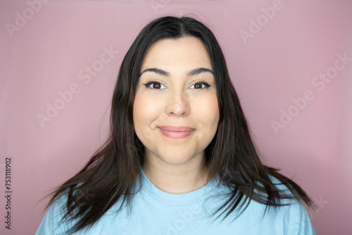 Close up image of an attractive young woman with long hair and a playful look, making an amused expression ina pink background
