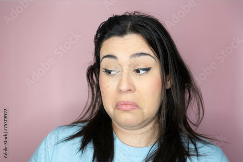 Close up image of an attractive young woman with long hair and a playful look, making an amused expression ina pink background photo