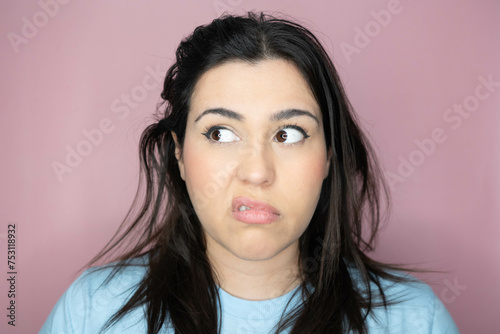 Close up image of an attractive young woman with long hair and a playful look, making an amused expression ina pink background photo