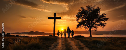 Silhouette of a family of parents and children walking together along a path towards a majestic wooden cross during a warm, orange sunset.