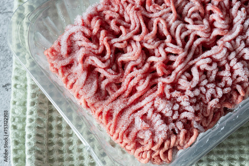 Frozen beef steak mince in a plastic container defrosting. On a green tea towel. photo