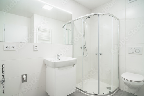 Bright white small bathroom with sink  wc and shower. The bathroom has a large mirror with LED strip  toilet flush button  heating ladder  few outlets and water with waste for the washing machine.