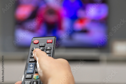 A woman's hand with a remote control switches channels on the TV. 