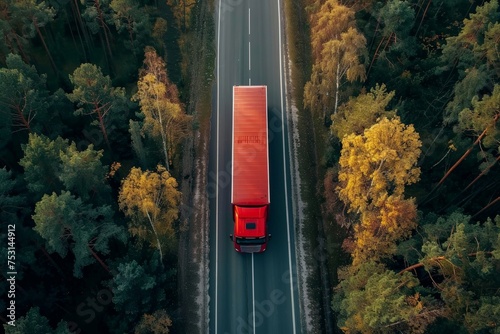 A red truck is driving down a road surrounded by lush green trees. The scene is captured from an aerial perspective, showcasing the transportation logistics background of the vehicle.