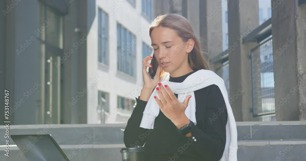 Young woman has hard business conversation with worker or subordinate while working on laptop sitting on building's stairs