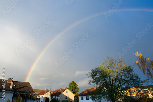 Panoramic view of rainbow with dark clouds over houses after a rainstorm