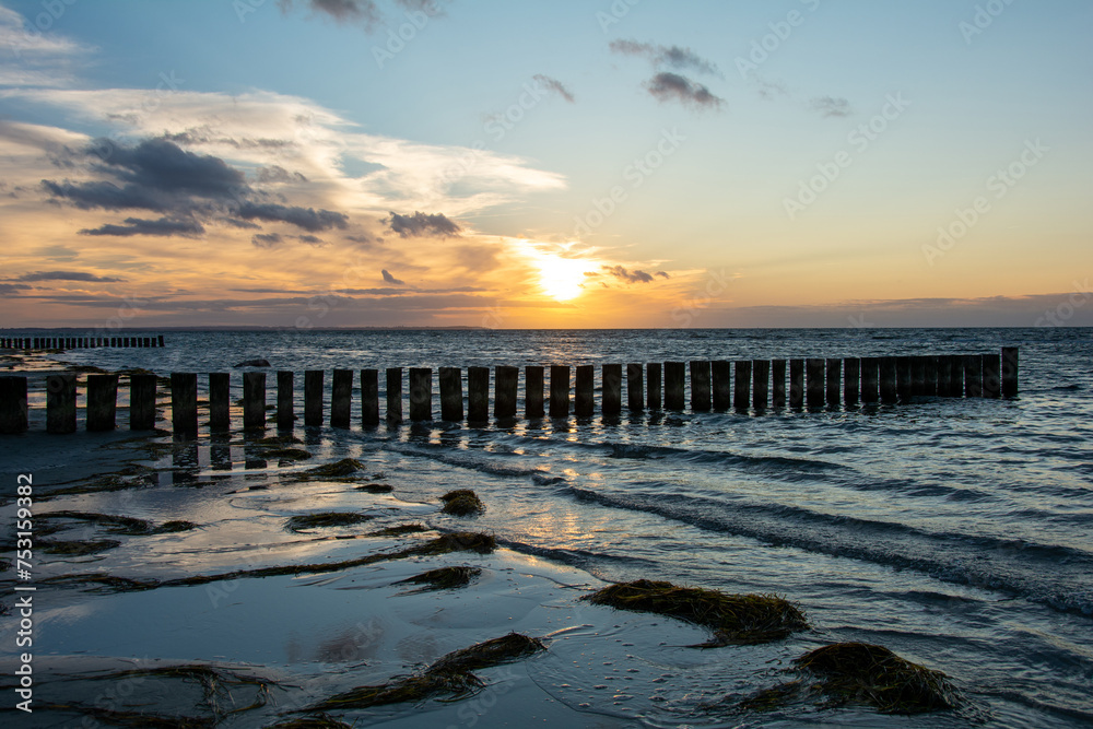 Sunset over the sea, with wooden groynes in the water