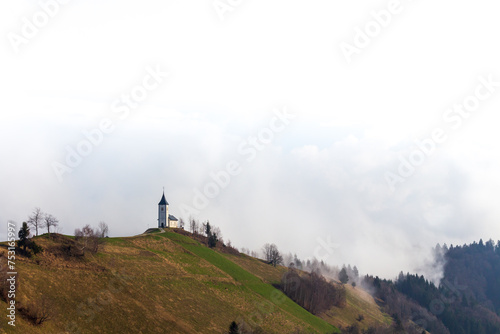 A scenic church slowly being surrounded by the thick white fog. A scenic church on top of the hill with old path leading to it. Church of saint Primoz and Felician - Jamnik - Slovenia. 