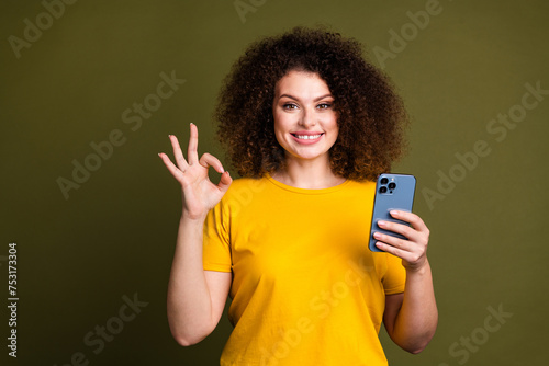 Portrait of attractive young woman wavy hair wear yellow basic t shirt demonstrate okey sign phone app isolated on khaki color background