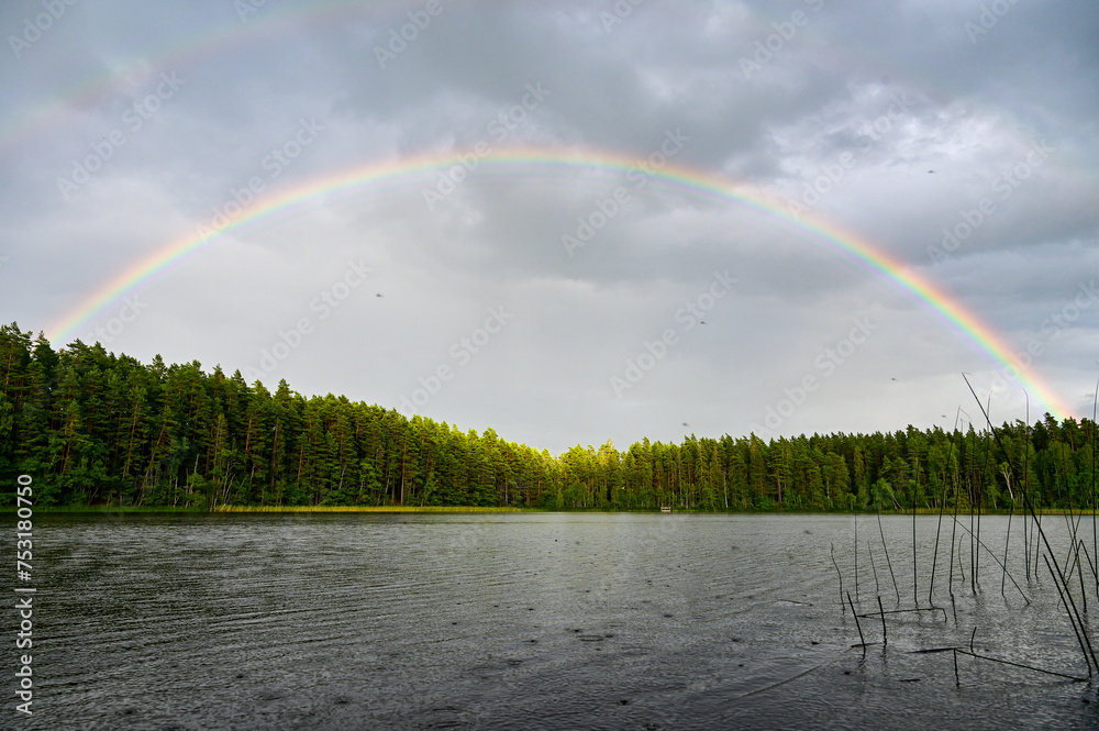 Double rainbow with main rainbow with interference arcs and secondary rainbows over Lake Helgasjön and trees in the background in Helgö National Park, Växjö, Kronobergs län, Smaland, Sweden - obrazy, fototapety, plakaty 