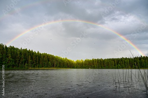 Double rainbow with main rainbow with interference arcs and secondary rainbows over Lake Helgasjön and trees in the background in Helgö National Park, Växjö, Kronobergs län, Smaland, Sweden photo