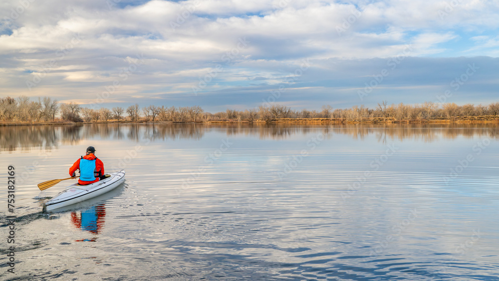 senior male paddler is paddling a decked expedition canoe on a calm lake in northern Colorado, winter scenery without snow