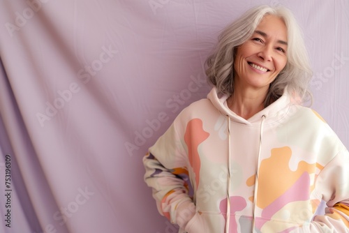 A playful senior woman laughs heartily in a kidcore-inspired, multicolor hoodie, her silver hair and joyful demeanor challenging age stereotypes. photo