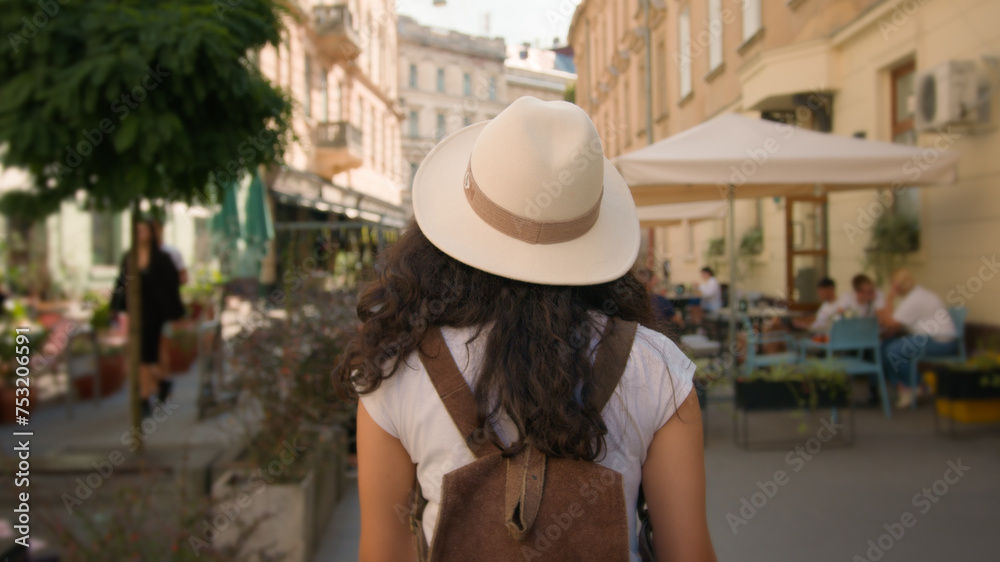 Walking outdoor cheerful smiling stylish Indian Arabian woman lady female tourist traveler follows back spinning turning have fun looking camera street explore town holidays journey vacations weekend