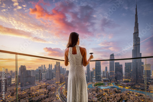 A elegant woman in a white evening dress enjoys the beautiful sunset view behind the modern skyline of Downtown Dubai, UAE