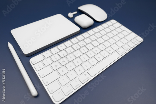 White keyboard, touchpad, mouse, earphones case and pen on dark blue background. Modern office, copy space. photo
