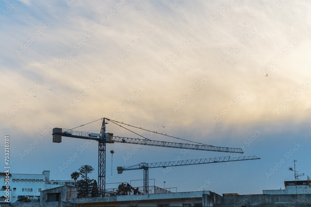 Two tower-type construction cranes on the background of a wide cyclonic cloud, changing weather conditions during various works