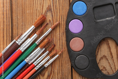 Watercolor paints with brushes on wooden background