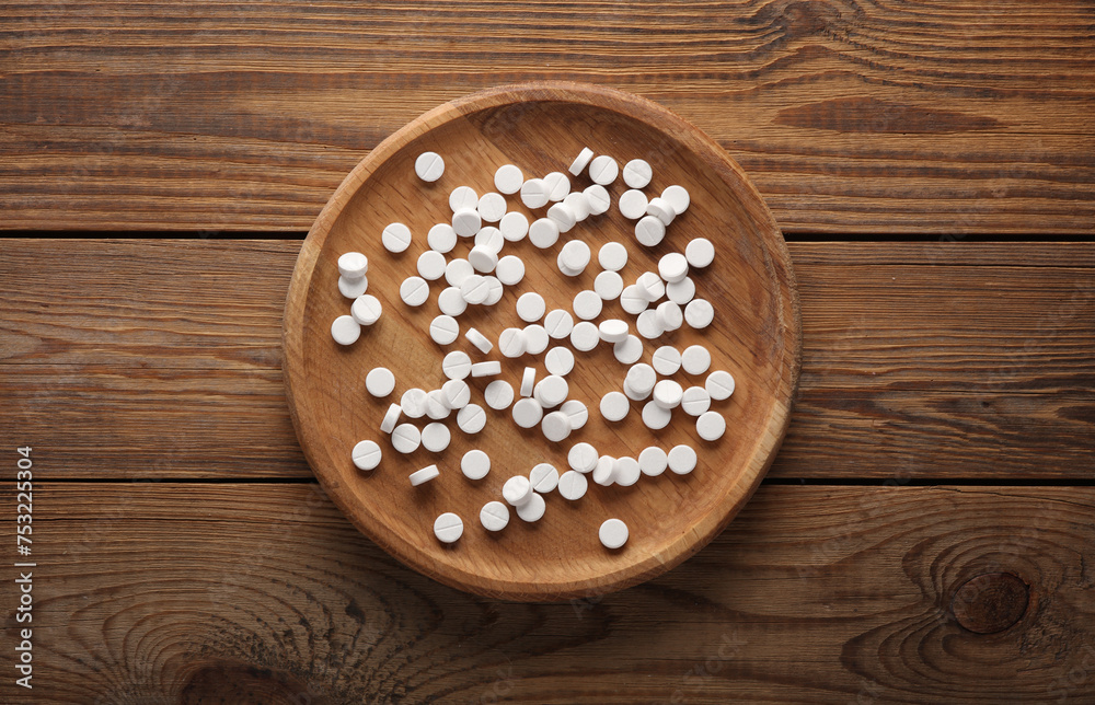 White pills with wooden plate on table.  Top view