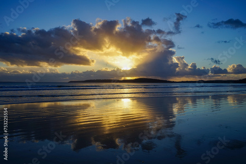 Les nuages se miroitent sur le sable humide à marée basse, peignant une toile céleste sur une plage de la Presqu'île de Crozon en Bretagne, offrant une vision saisissante de la nature.