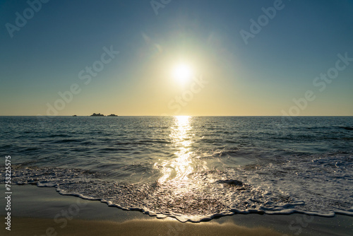 Soleil éclatant en fin de journée sur une plage bretonne, sous un ciel bleu reflétant dans la mer et sur le sable.