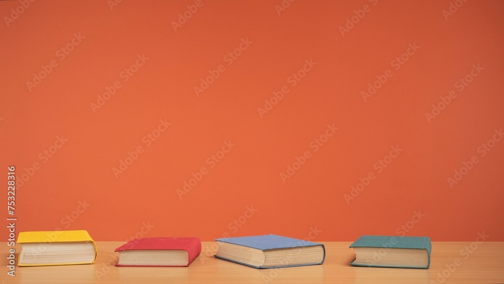 Old books with colored covers on a wooden table on a bright orange background. Old books with colored covers on a wooden table on a bright orange background.