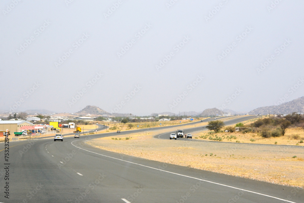 Fototapeta premium Car view of a winding asphalt road in the desert in perspective with cars driving ahead under a blue sky