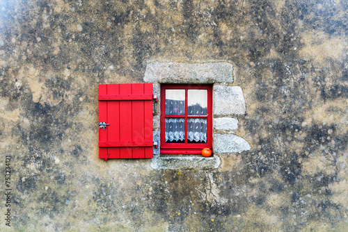 Un mur de pierre solide encadre une fenêtre à petits carreaux, agrémentée d'un volet rouge éclatant, créant une image pittoresque et charmante évoquant le style architectural typique des maisons de ca © Laurent