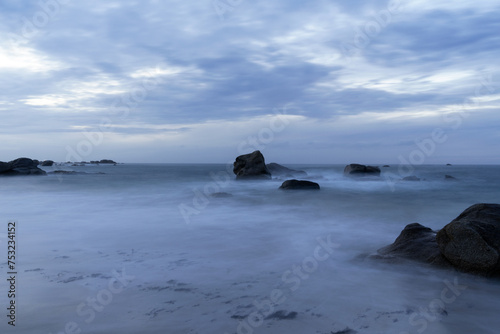 Pose longue capturant la tranquillité d'une plage bretonne sous un ciel couvert, fusionnant les éléments pour une scène à la fois calme et mystérieuse.