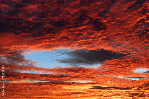 Red cloudscape with blue fallstreak hole in cirrocumulus clouds at evening twilight. Beautiful fiery afterglow on orange sky with unusual cavum at wonder winter sunset. Impressive elliptical skypunch.