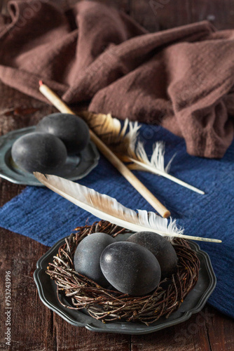 Wine painted eggs in a nest, bird feathers, drapery on a wooden background. Easter concept.