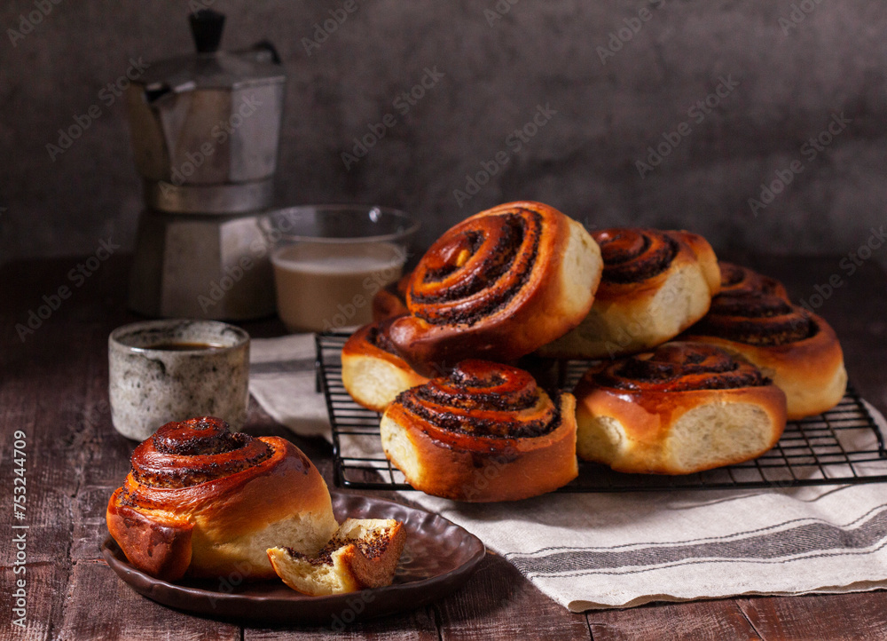 Yeast dough cinnabons with poppy seeds, raisins and candied fruits, served with coffee. Rustic style.