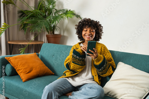 African girl holding smartphone touch screen typing scroll page at home. Woman with cell phone surfing internet using social media apps playing game. Shopping online Internet news cellphone addiction